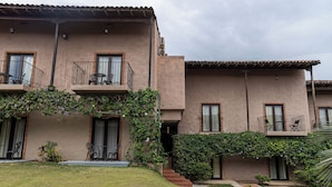 A two-story building with a flat roof, balconies with metal railings, and a small garden area with grass and plants. - Hotel Cubitá Boutique Resort & Spa (La Arena)