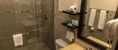 A bathroom with a glass-enclosed shower, a toilet, a sink with a mirror, and shelves with toiletries.