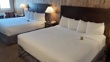 A hotel room with two beds, each with white linens and pillows, a wooden headboard, bedside lamps, and a small nightstand with a phone.