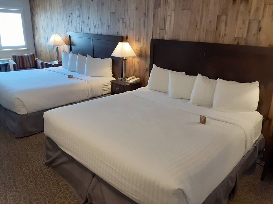 A hotel room with two beds, each with white linens and pillows, a wooden headboard, bedside lamps, and a small nightstand with a phone.