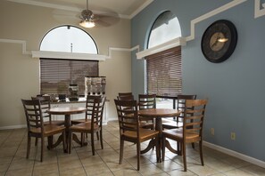 A dining area with a round table and six chairs, a kitchen in the background, and a clock on the wall. - Mission Inn (Santa Cruz)