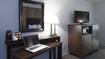 A hotel room with a wooden desk, a laptop, a television, a lamp, and a minibar.