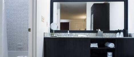 Un baño moderno con tocador oscuro, un espejo grande y toallas dobladas con cuidado.