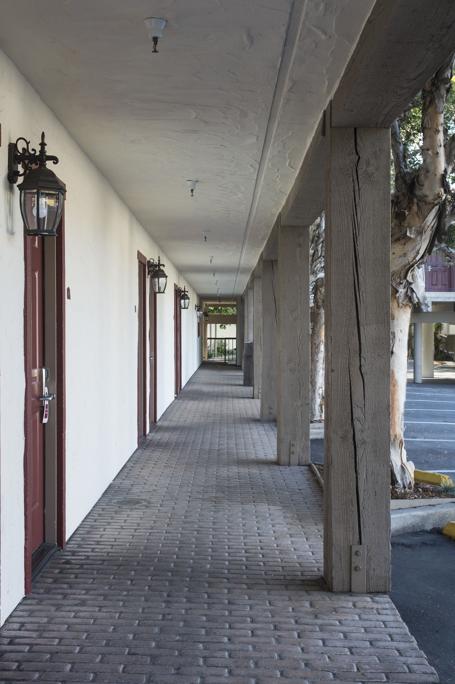 A covered corridor with brick flooring, wooden pillars, and doors with glass panels.