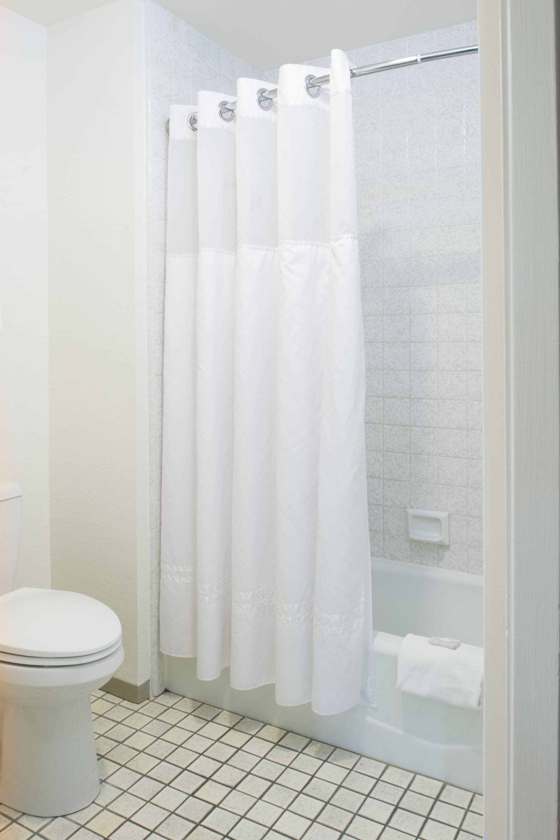 A bathroom with a white toilet, a shower with a white curtain, and a tiled floor.