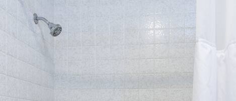 Une salle de bain aux murs recouverts de carreaux blancs, avec une baignoire, une pomme de douche et un porte-savon.
