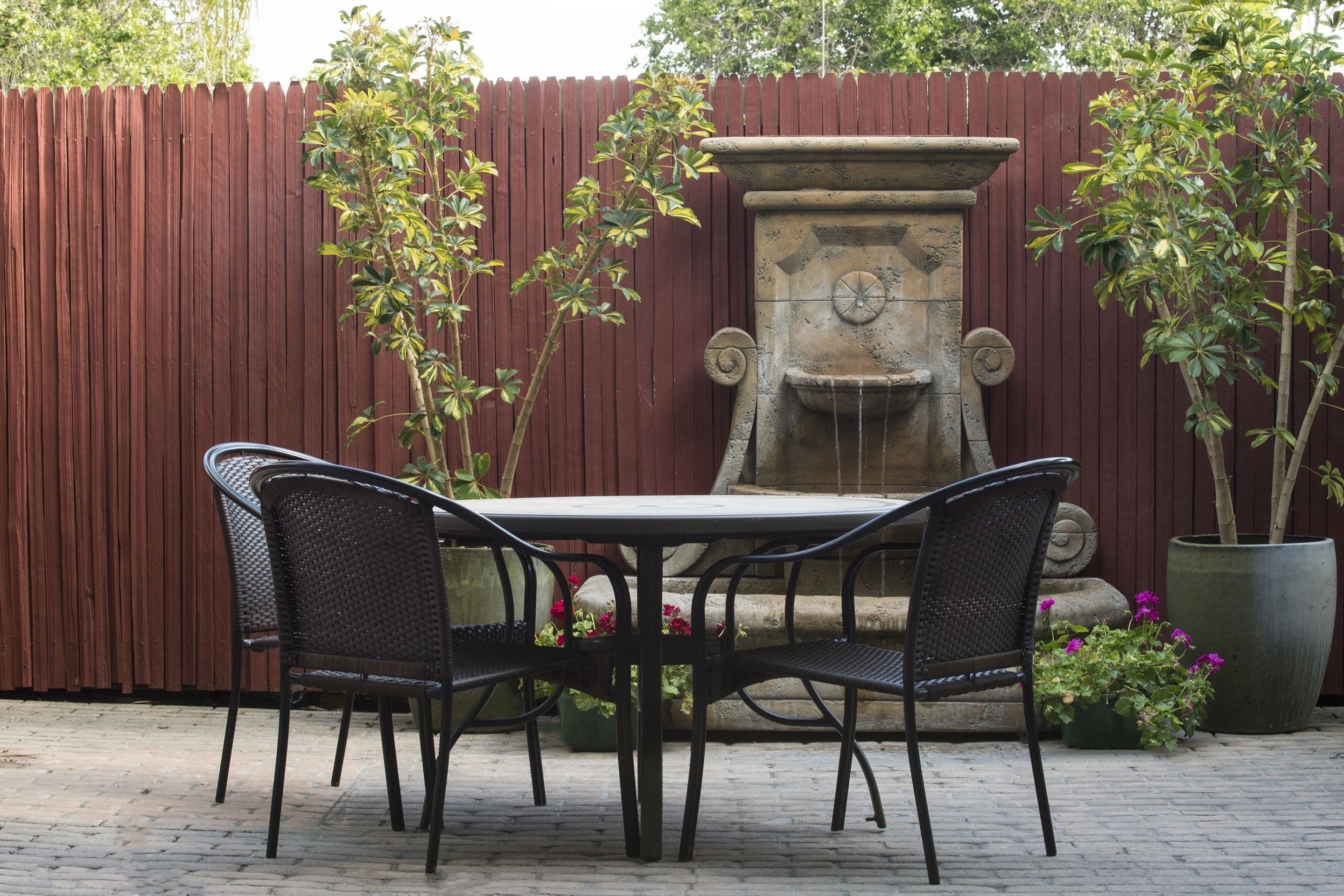 A patio with a table and chairs, a decorative stone fountain, and potted plants.