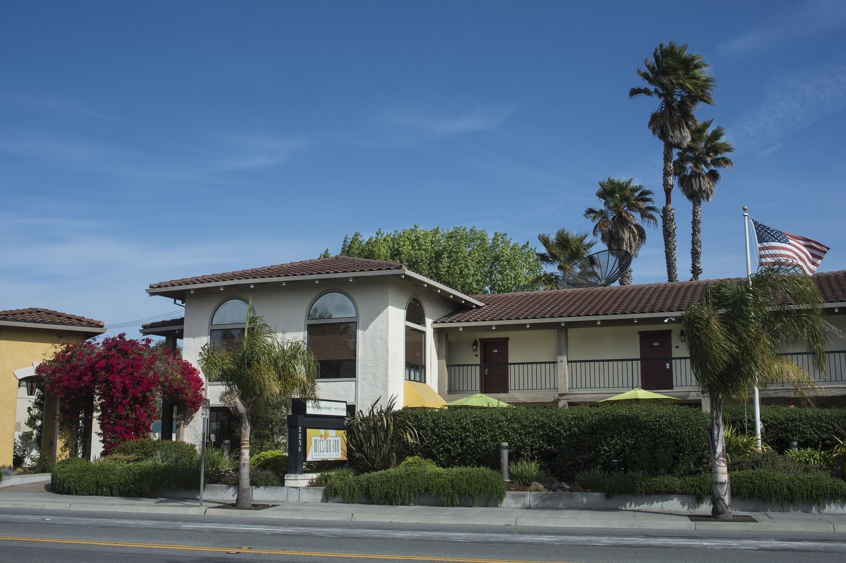 A hotel with a two-story structure, a red-tiled roof, and a flag on the right.