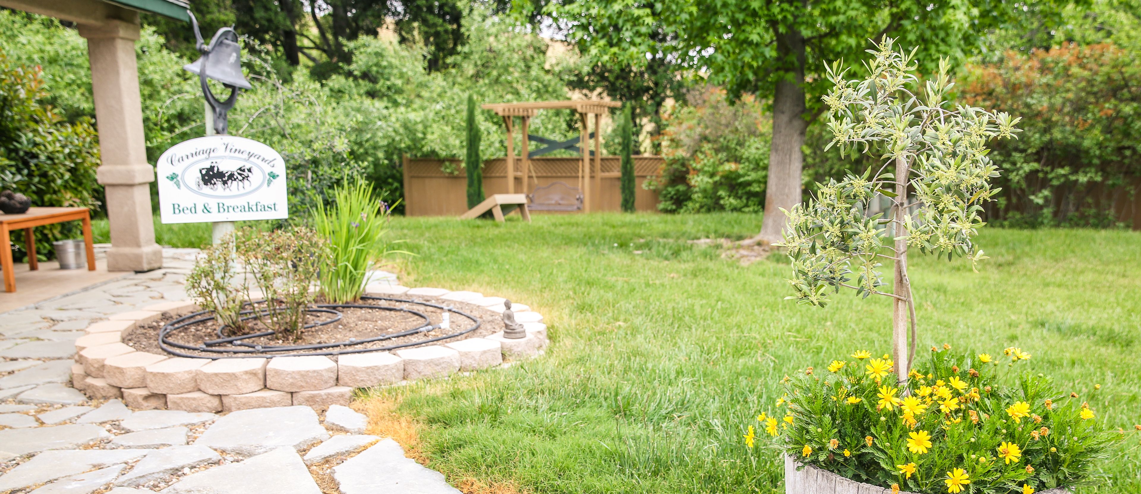 Un espace aménagé en jardin, avec un panneau indiquant « Carriage Vineyards Bed & Breakfast », une petite statue et un parterre de fleurs aux fleurs jaunes.