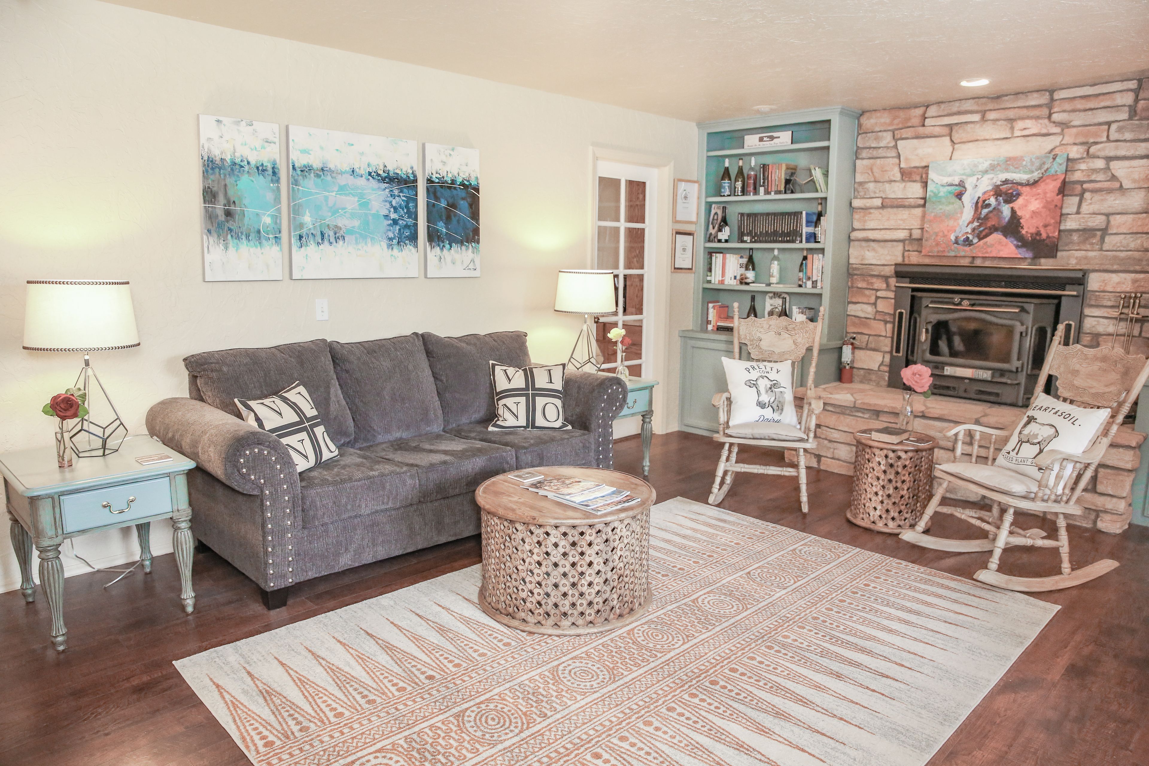 A cozy living room with a grey sofa, a round coffee table, a bookshelf, and a fireplace.