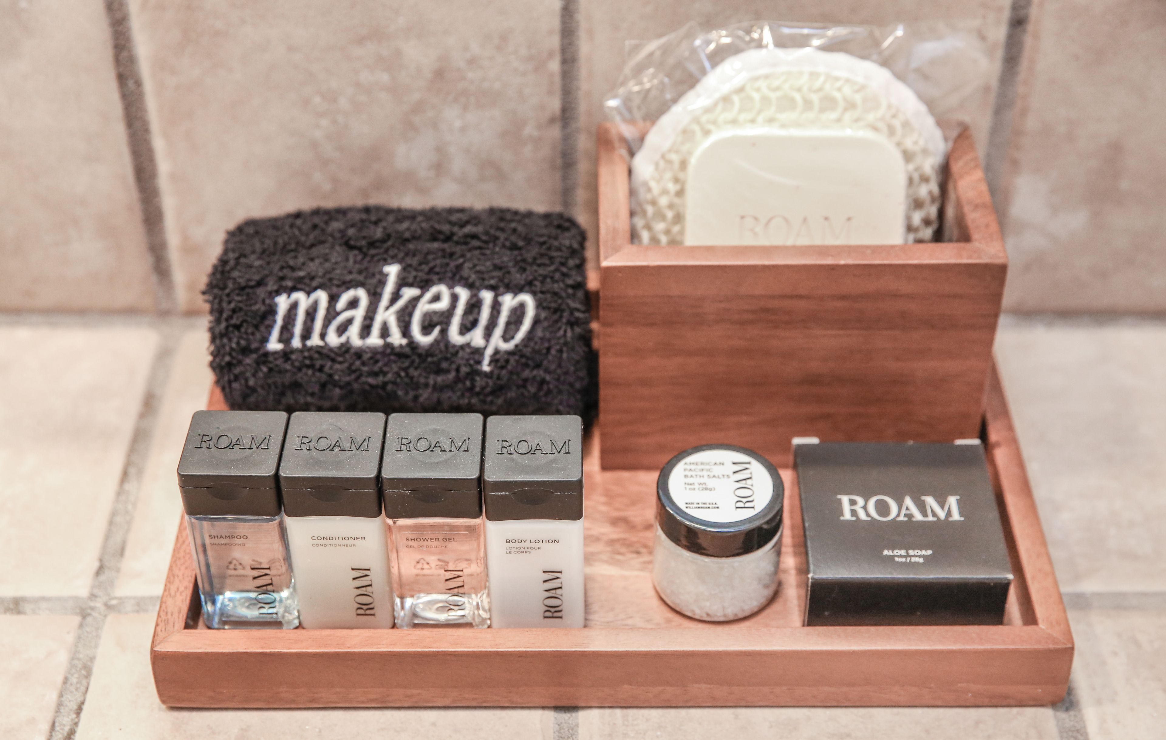 A wooden tray with ROAM brand toiletries including shampoo, conditioner, shower gel, body lotion, and aloe soap.