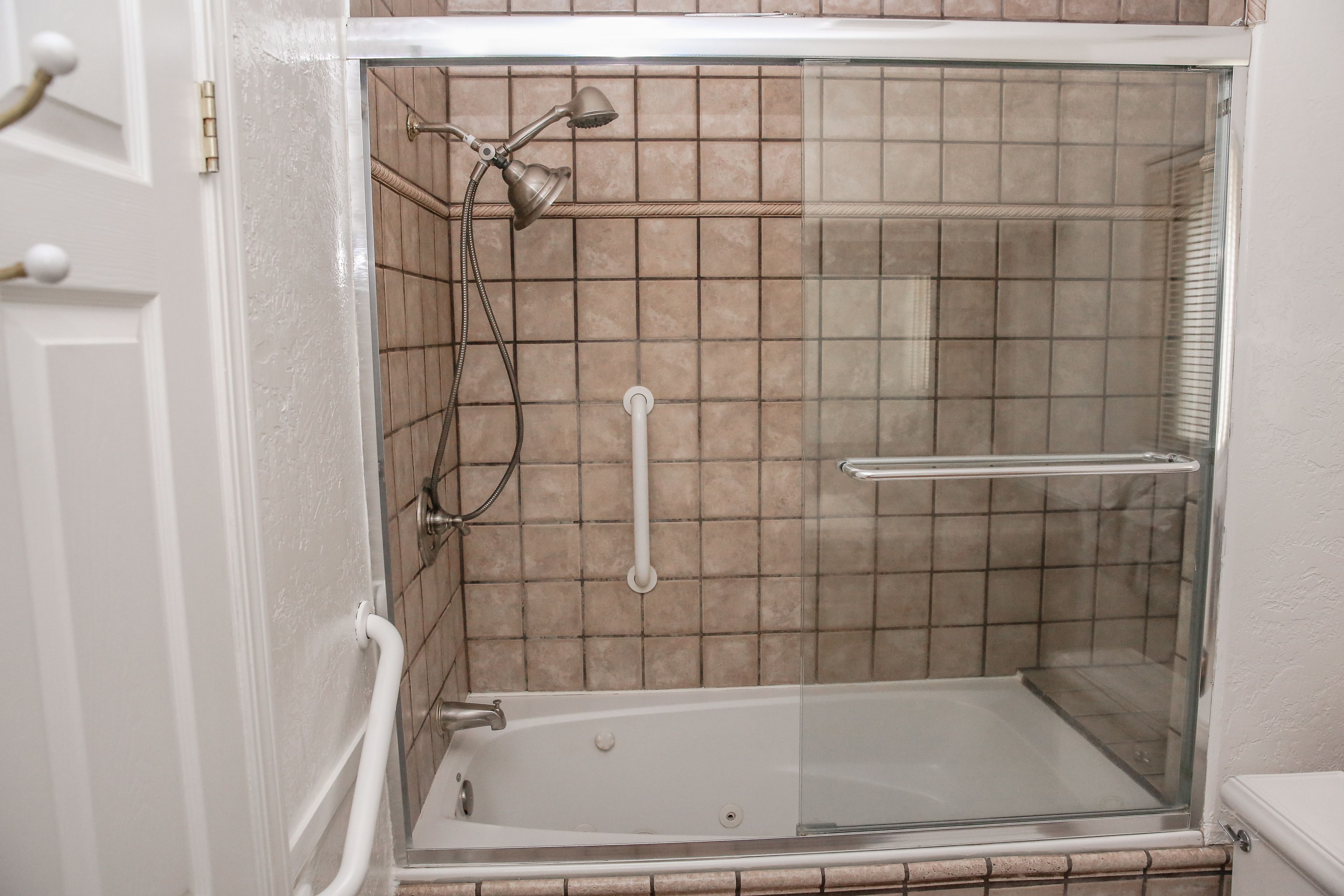 A walk-in shower with a glass door, a handheld showerhead, and a handheld shower attachment.