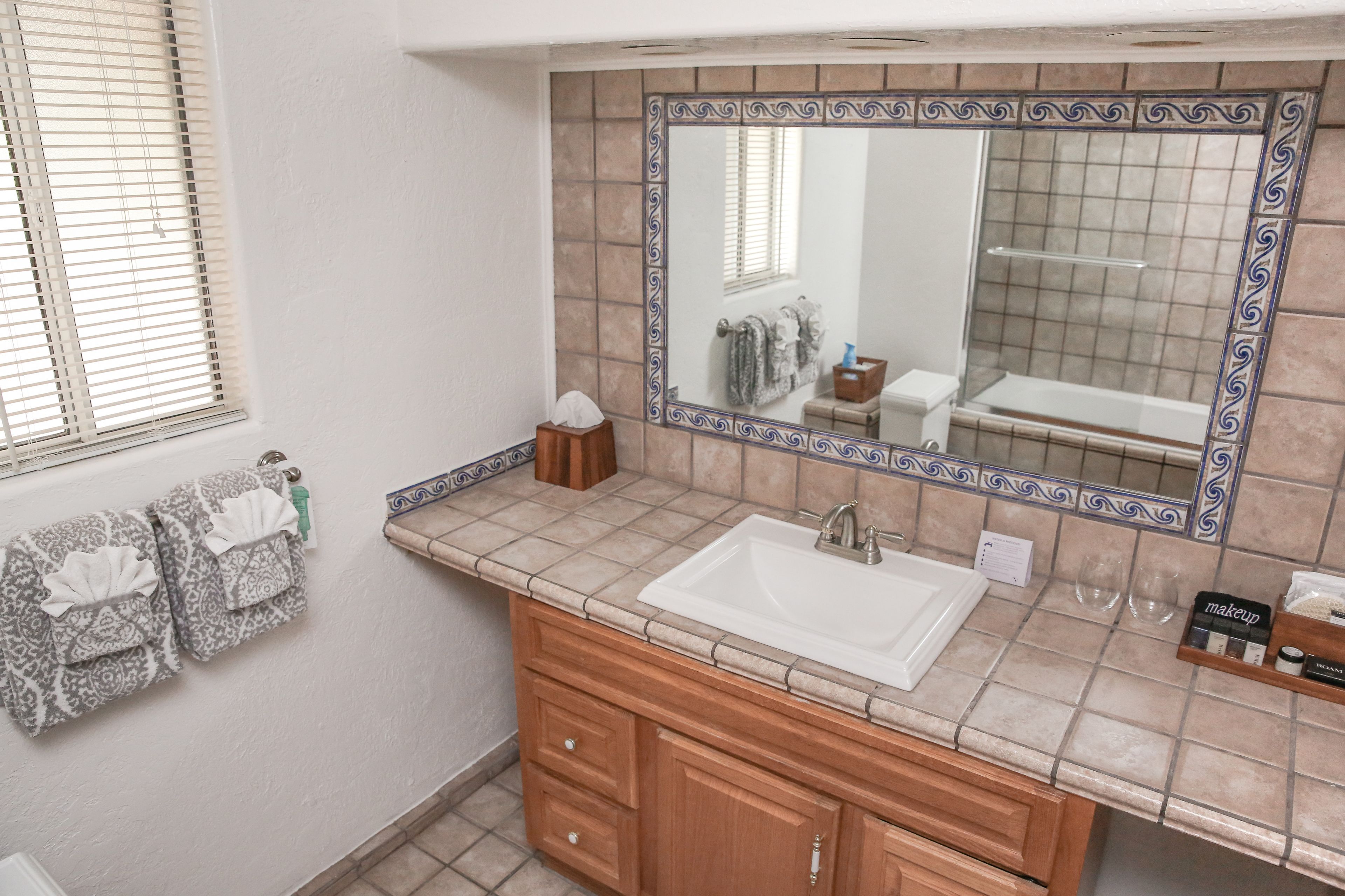 Un baño con lavamanos blanco, tocador de madera y un espejo grande con azulejos decorativos.