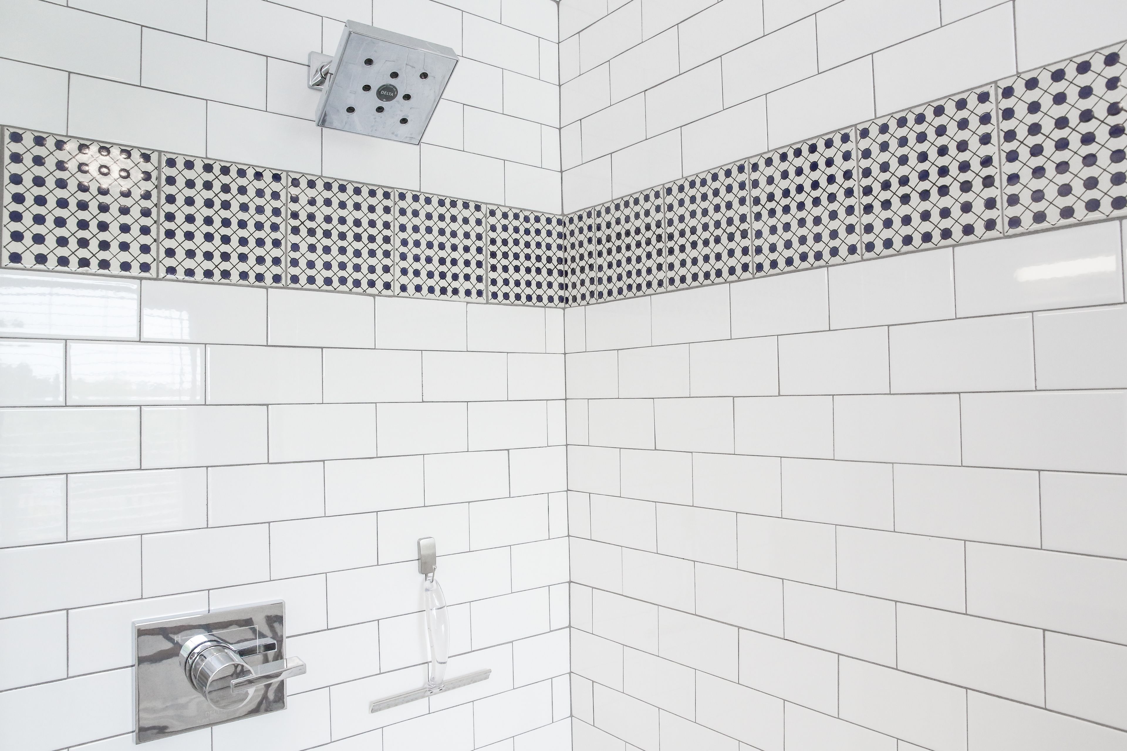 A corner of a bathroom with white subway tiles, a metal vent, and a chrome towel rack.