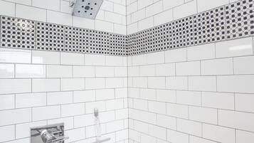 A corner of a bathroom with white subway tiles, a metal vent, and a chrome towel rack.