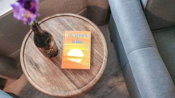 A book titled "The Teaching of Buddha" on a wooden side table with a vase of purple flowers.