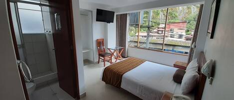 Una camera d'albergo con un letto, una scrivania, una sedia, una TV e un bagno.