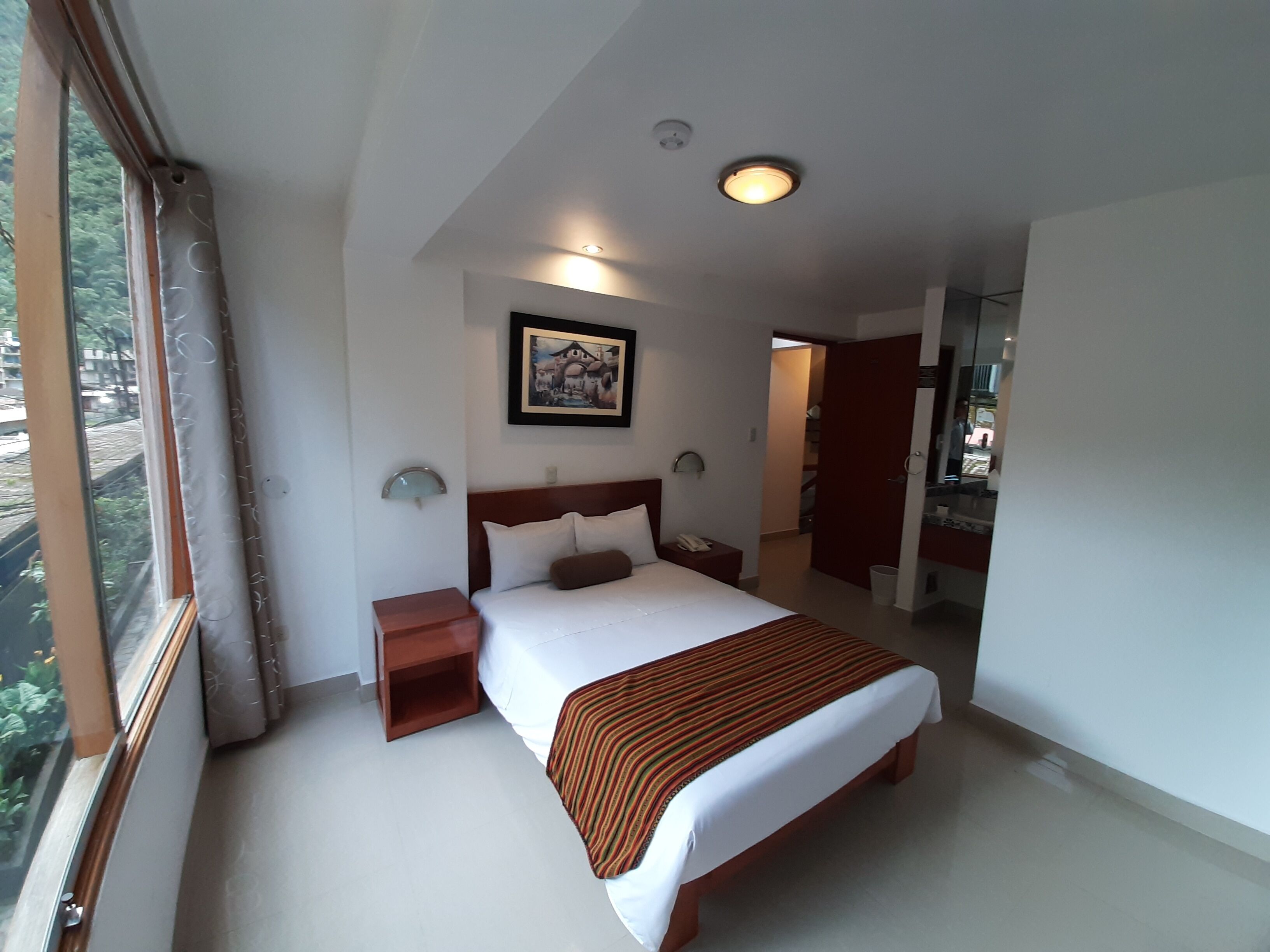 Habitación de hotel moderna con una cama grande, mesitas de noche, un cuadro en la pared y vistas a través de la ventana.