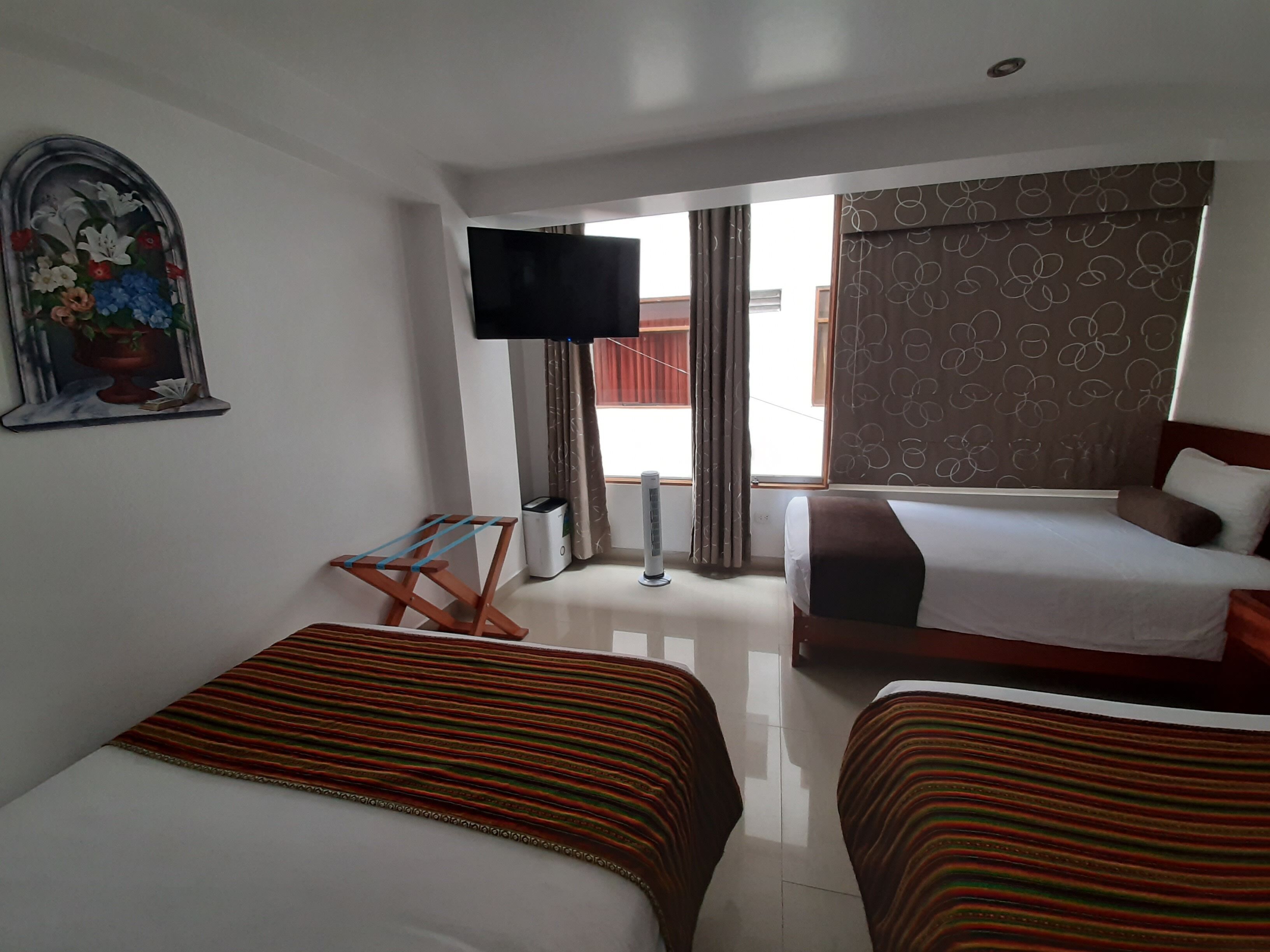 A hotel room with two beds, a TV, a painting, and a window with curtains.