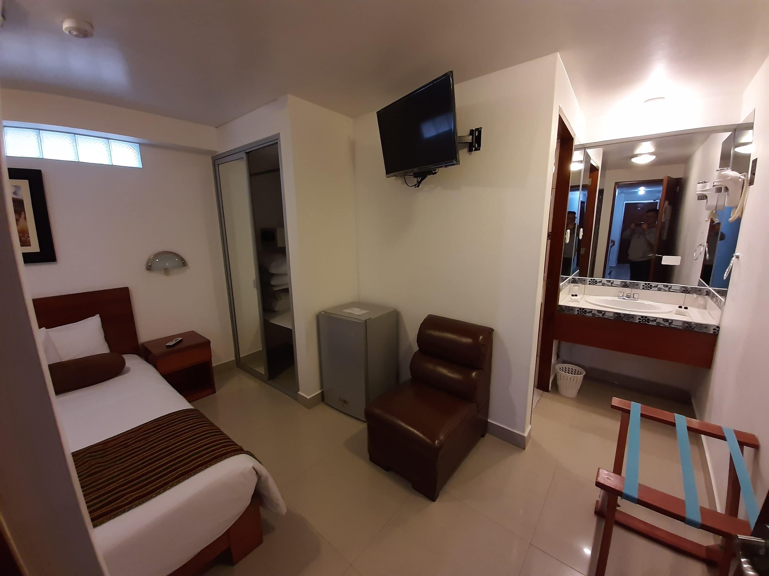 Une chambre d’hôtel comprenant un lit, un bureau, une chaise, une télévision, une salle de bain avec un miroir et une fenêtre.