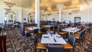 A spacious restaurant with high ceilings, modern lighting, and a patterned carpet. Tables are set with glasses and cutlery.