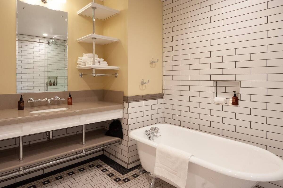Ein Badezimmer mit einer weißen Badewanne, zwei Waschbecken, einem Spiegel und einer gefliesten Rückwand.