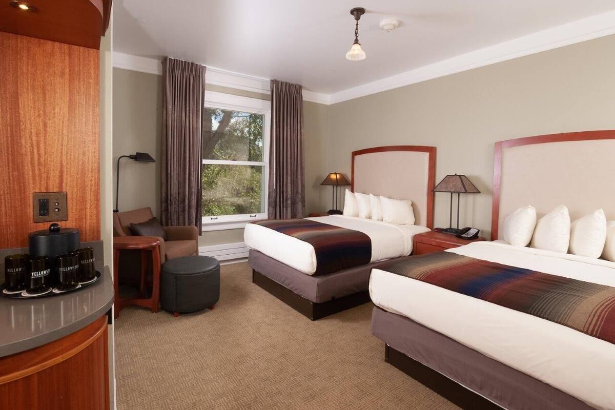 Ein Hotelzimmer mit zwei Betten, einem Holztisch mit Kaffeemaschine, einem Stuhl und einem fenster mit Vorhängen.