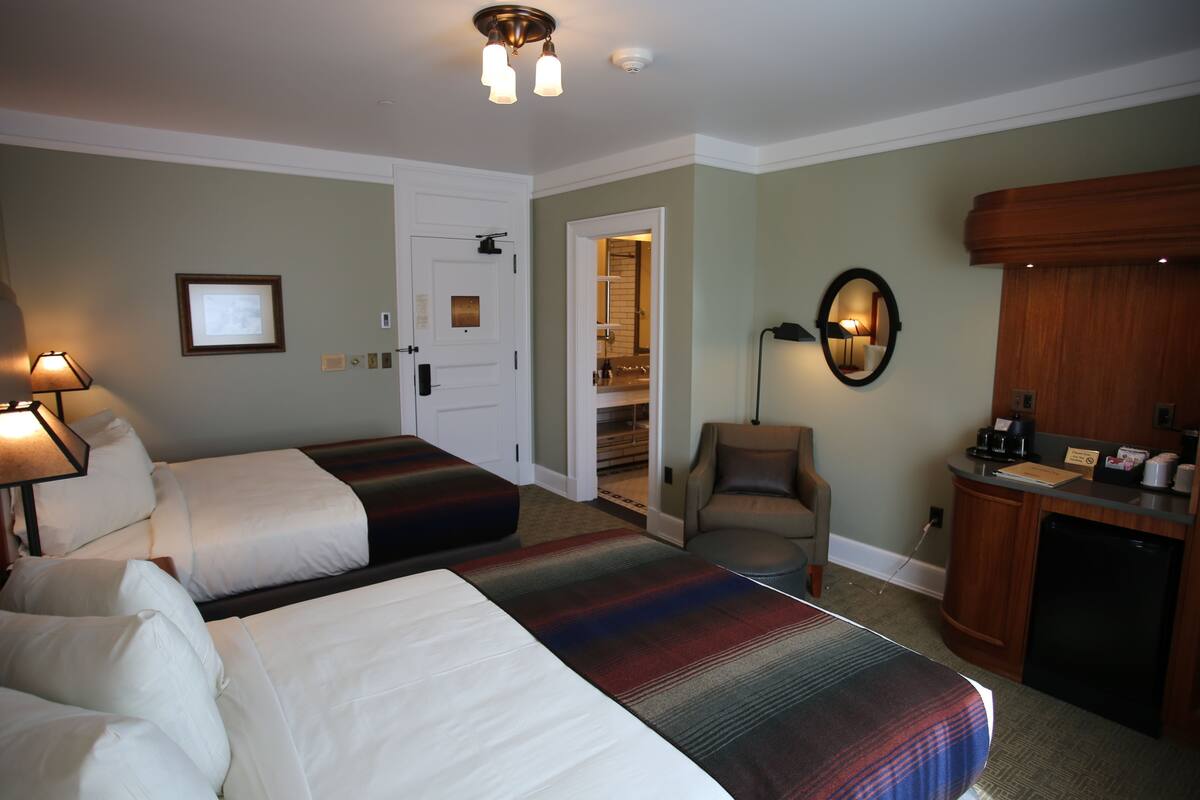 Ein Hotelzimmer mit zwei Betten, einem Schreibtisch, einem Stuhl, einem Spiegel und einer Tür zu einem Badezimmer.