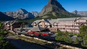 A lodge with multiple floors, a parking area with red vehicles, and a backdrop of mountains and a lake.