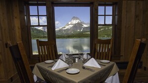 A dining table set for two with a mountain view through large windows. - Many Glacier Hotel - Inside the Park (East Glacier Park)