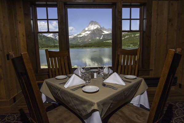 A dining table set for two with a mountain view through large windows. - Many Glacier Hotel - Inside the Park (East Glacier Park)