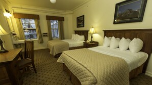 A hotel room with two beds, a desk, a chair, a lamp, and a framed picture on the wall.