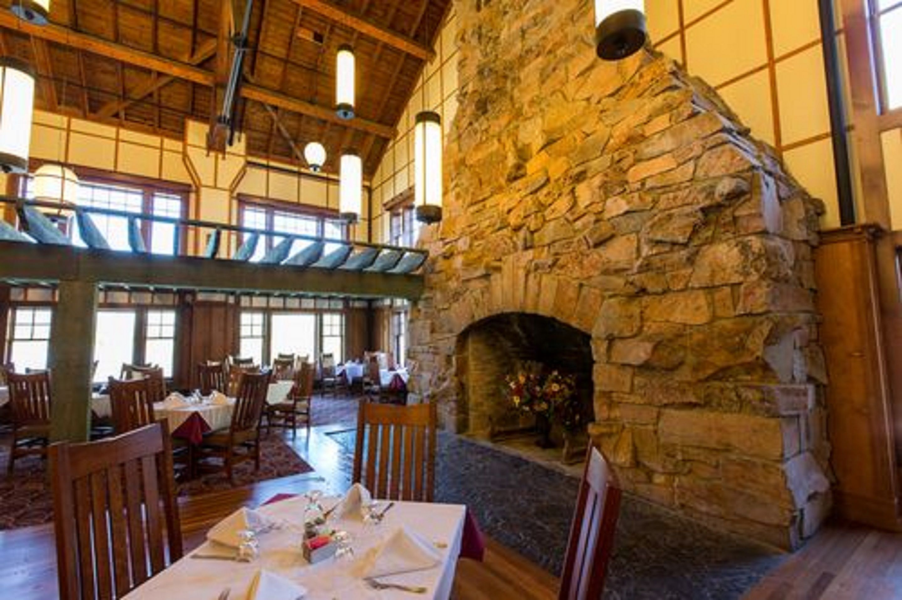 A spacious dining area with a stone fireplace, wooden beams, and large windows.