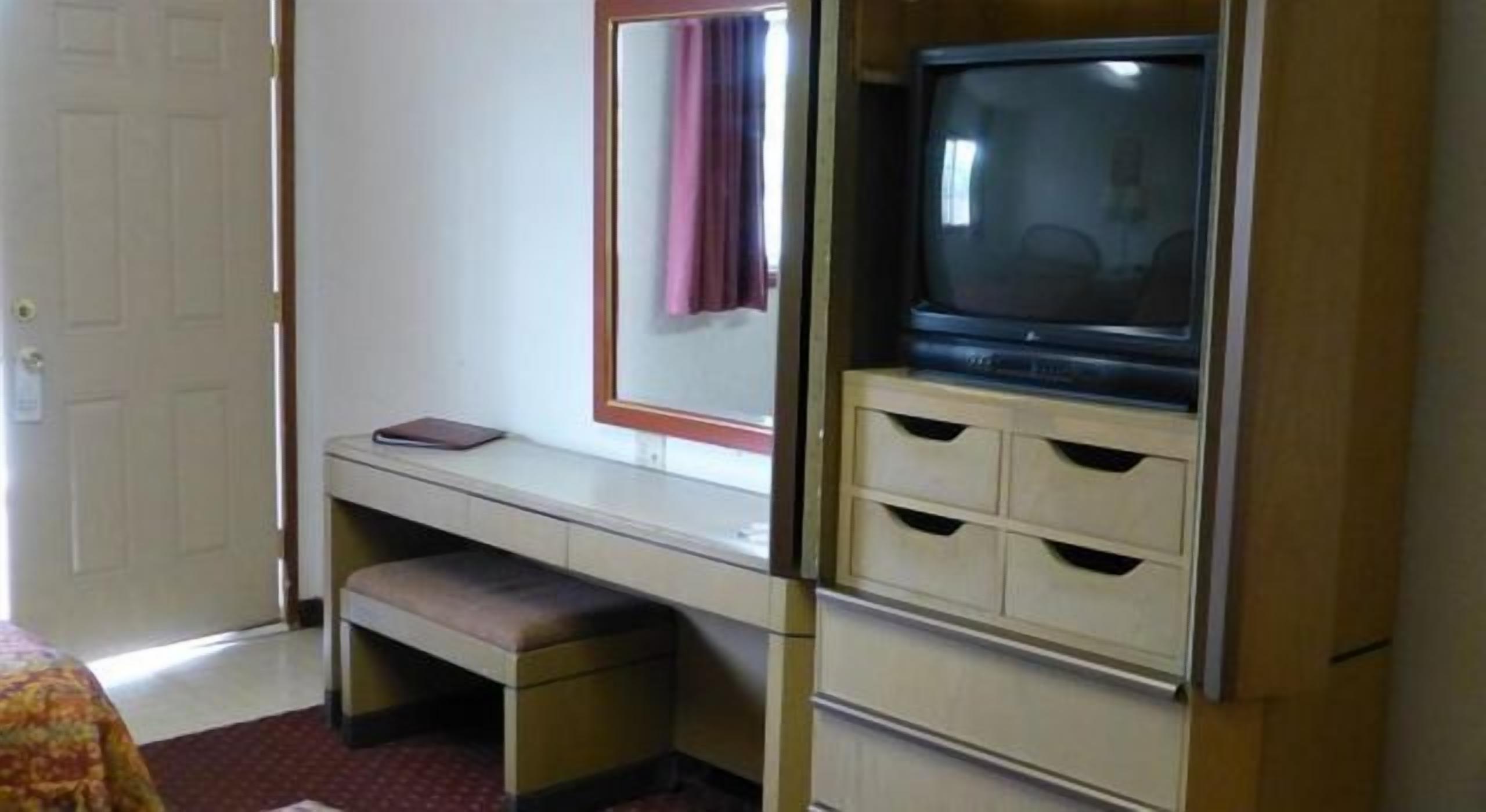 Una habitación pequeña con escritorio, televisión y una banca.