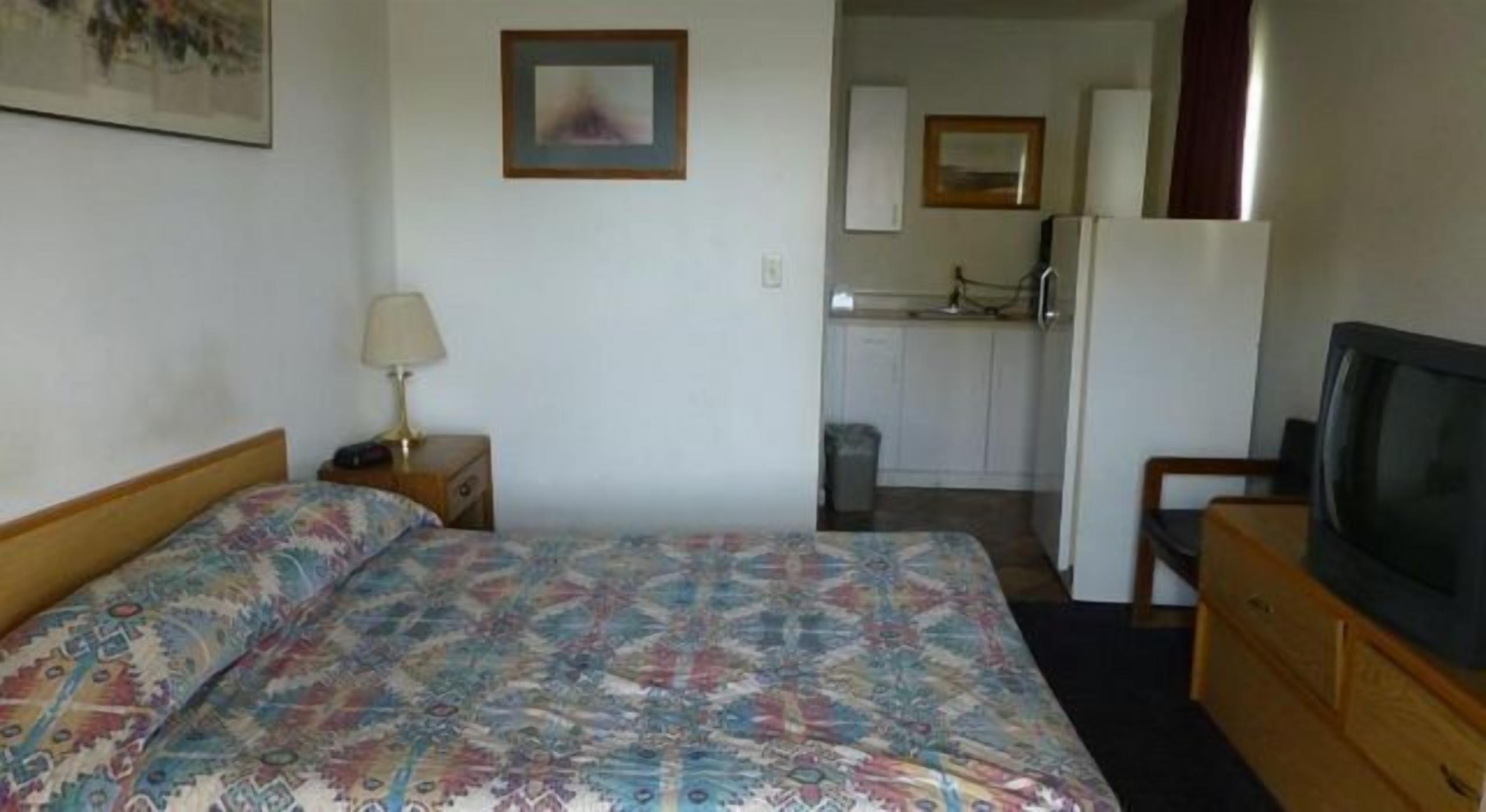 A hotel room with a bed, a desk, a television, a kitchenette, and a bathroom.
