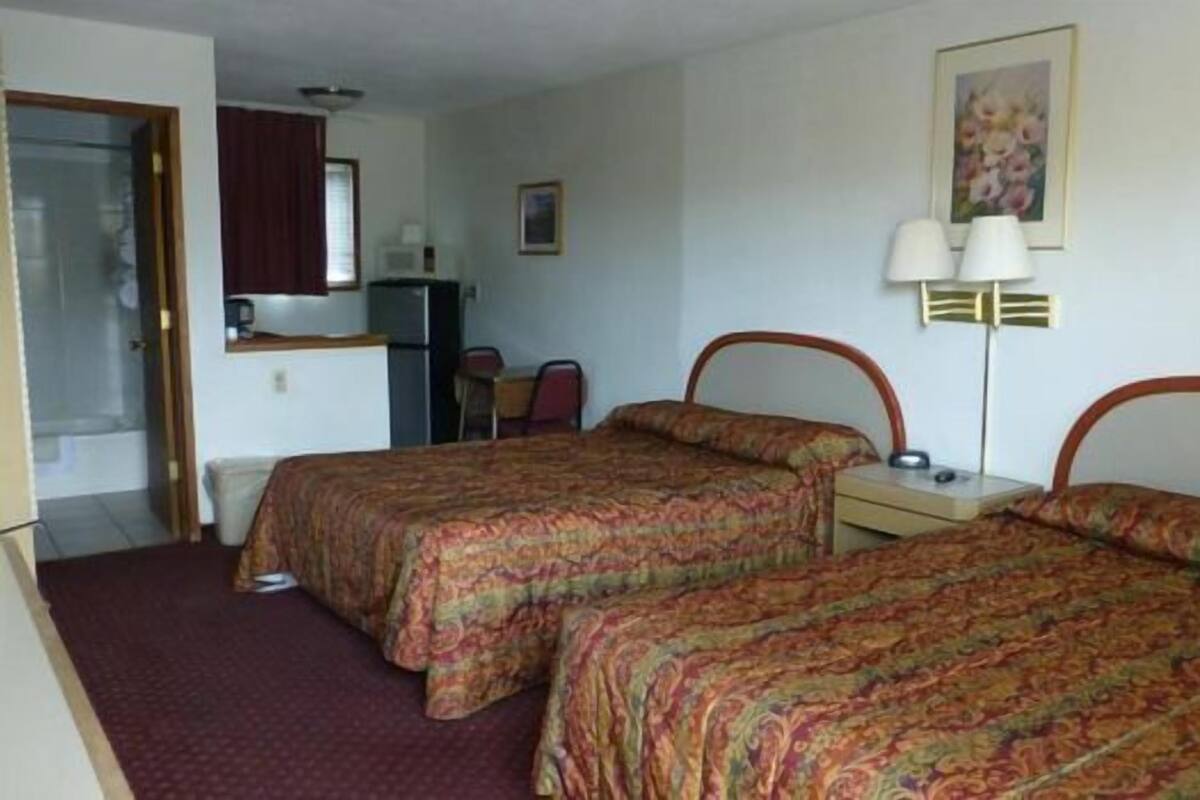 A hotel room with two beds, a desk, a chair, a refrigerator, and a painting on the wall.