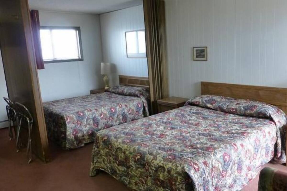 A room with two beds, a wooden headboard, a nightstand with a lamp, and a small table.