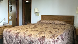 A hotel room with a large bed, a wooden headboard, a bedside lamp, a nightstand, and a door leading to another room. - Umatilla Inn and Suites (Umatilla)