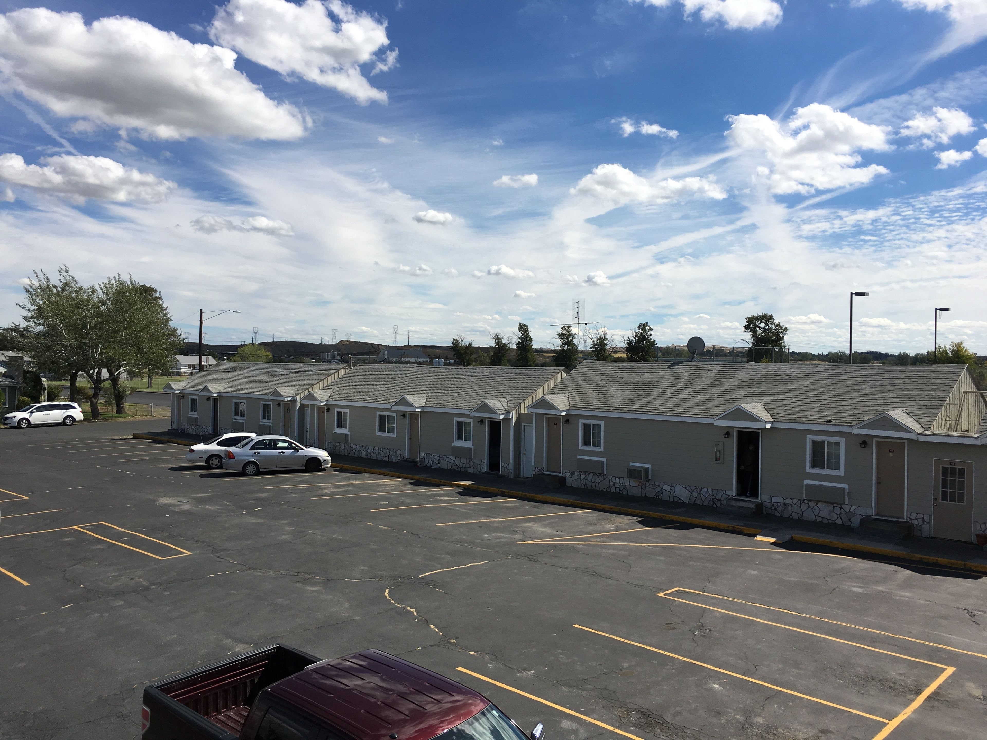 A parking lot with several cars, a building with a sloped roof, and a clear sky with clouds.