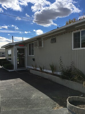 A small, single-story building with a 'OPEN' sign, a welcoming 'WELCOME' sign, and a number '1370' on the door.