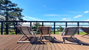 Une terrasse en bois avec trois chaises longues donnant sur un paysage magnifique, avec l’océan et les arbres en toile de fond.