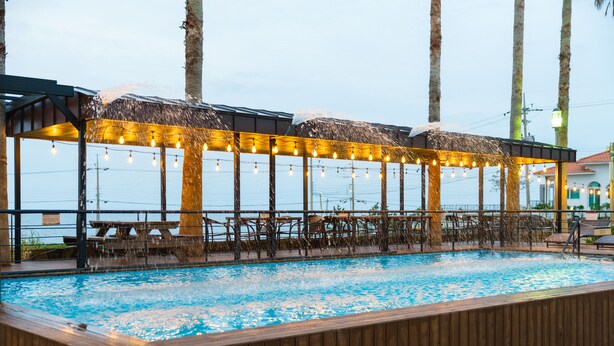 Un espace piscine extérieur doté d’une terrasse en bois, de chaises longues et de guirlandes lumineuses.