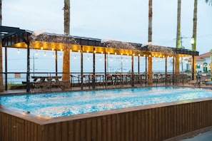 Un espace piscine extérieur doté d’une terrasse en bois, de chaises longues et de guirlandes lumineuses.