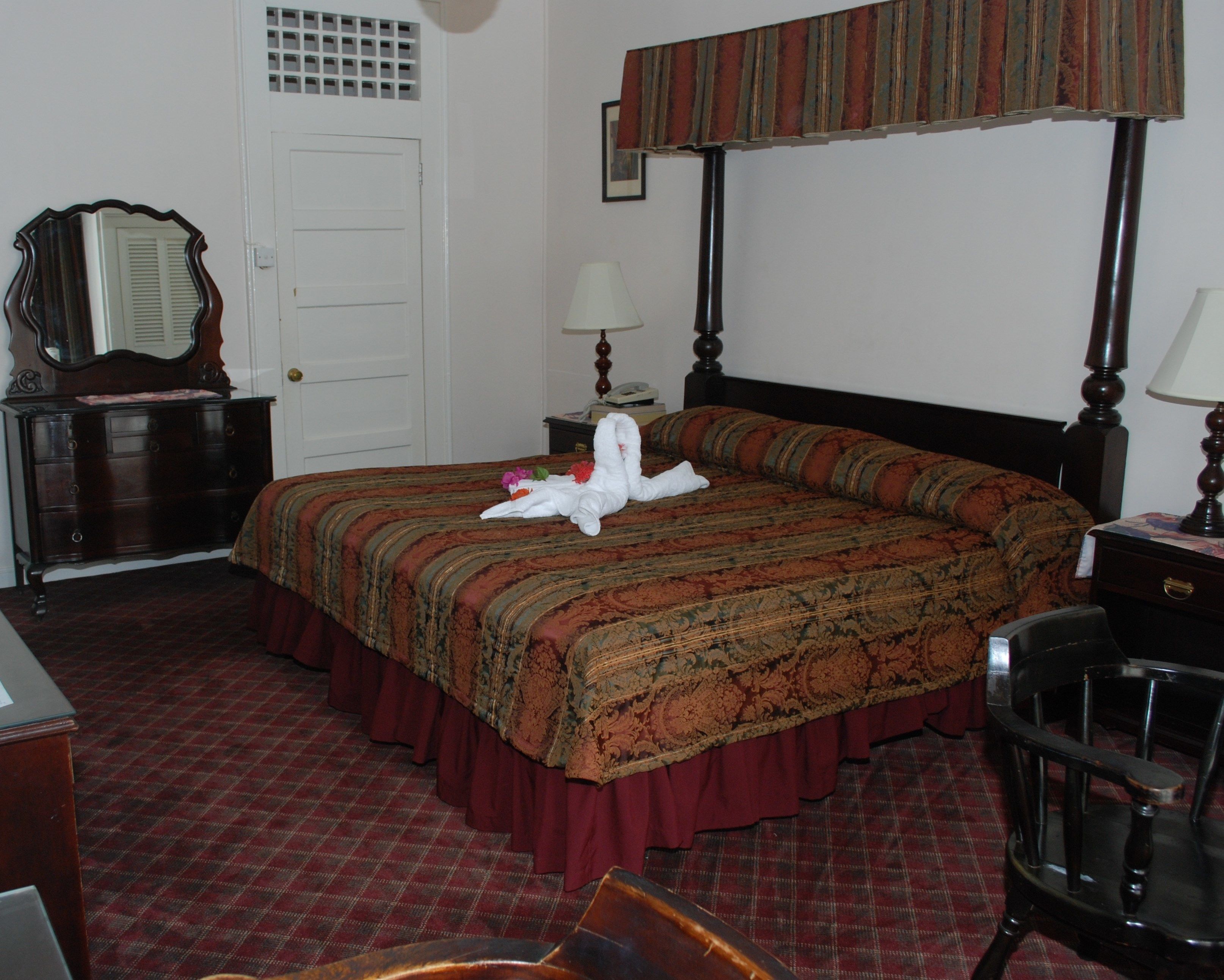 Quarto de hotel com cama de dossel, cómoda, escrivaninha e uma cadeira.
