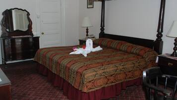 Quarto de hotel com cama de dossel, cómoda, escrivaninha e uma cadeira.