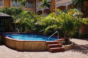 Una piscina rodeada por un paseo de ladrillo, palmeras y un edificio con balcones.
