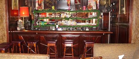 A bar area with wooden bar stools, a counter with various bottles, and Christmas decorations.