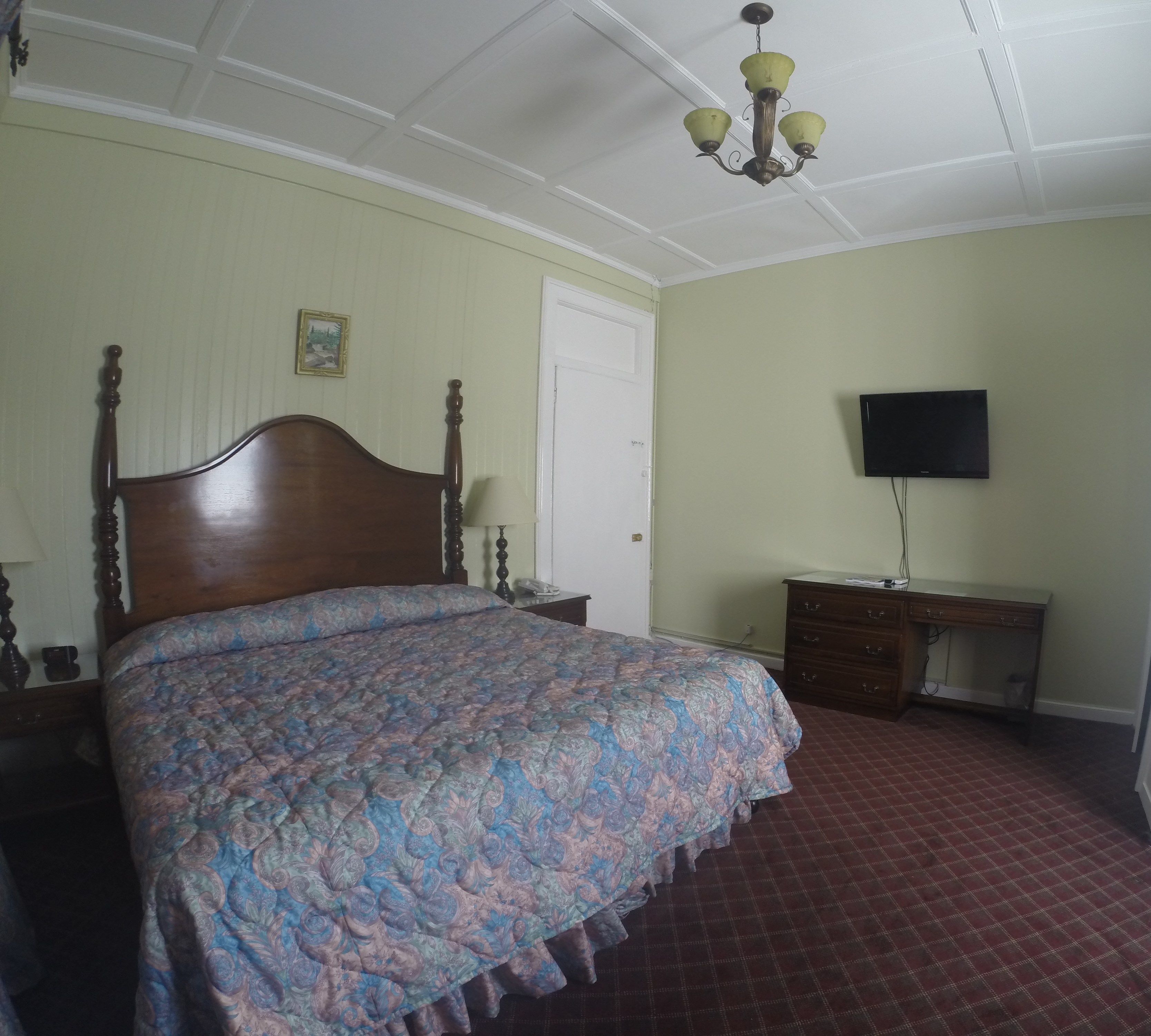 A bedroom with a wooden bed, a nightstand, a dresser, a television, and a chandelier.