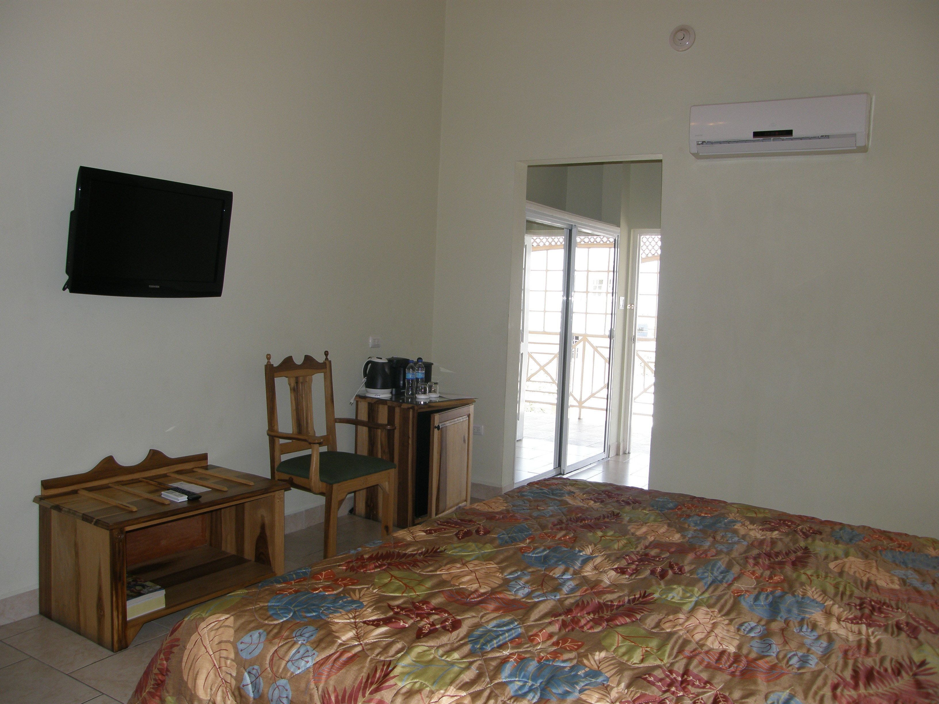 A bedroom with a bed, a desk, a chair, a television, and a sliding glass door leading to a balcony.