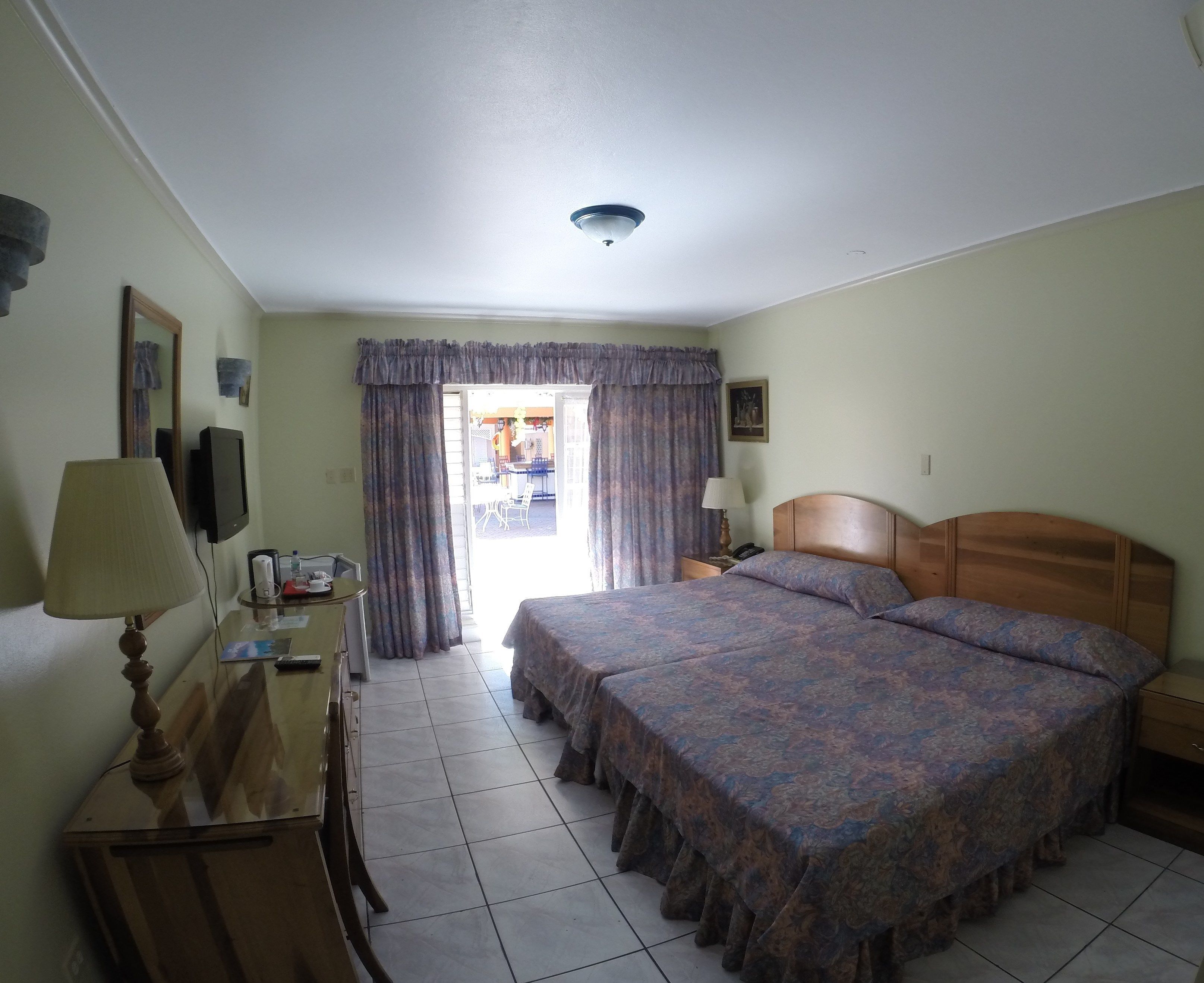 Habitación de hotel con cama, mesita de noche, lámpara y vistas al exterior.